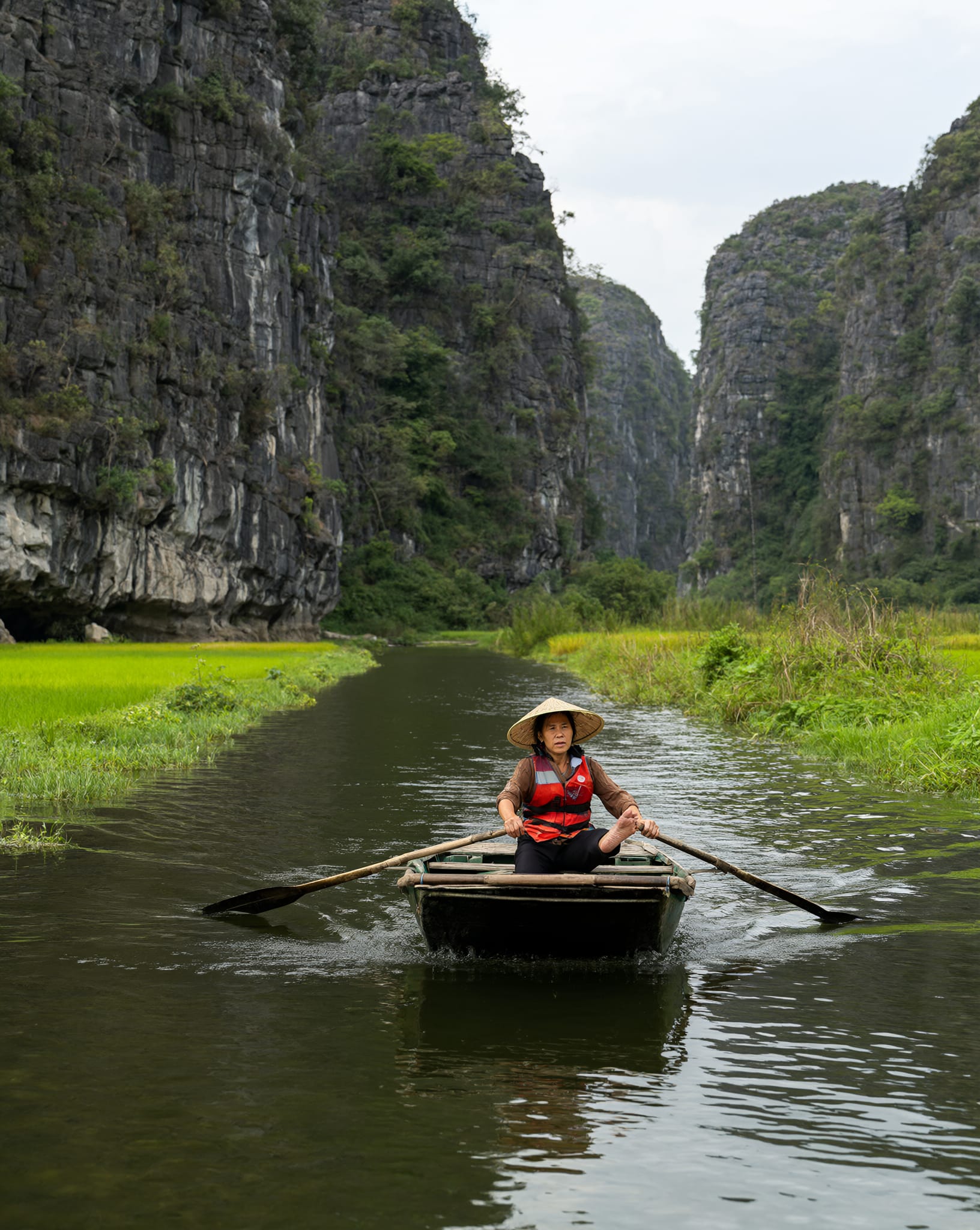 A rower paddles a sampan between Ninh Binh limestone cliffs